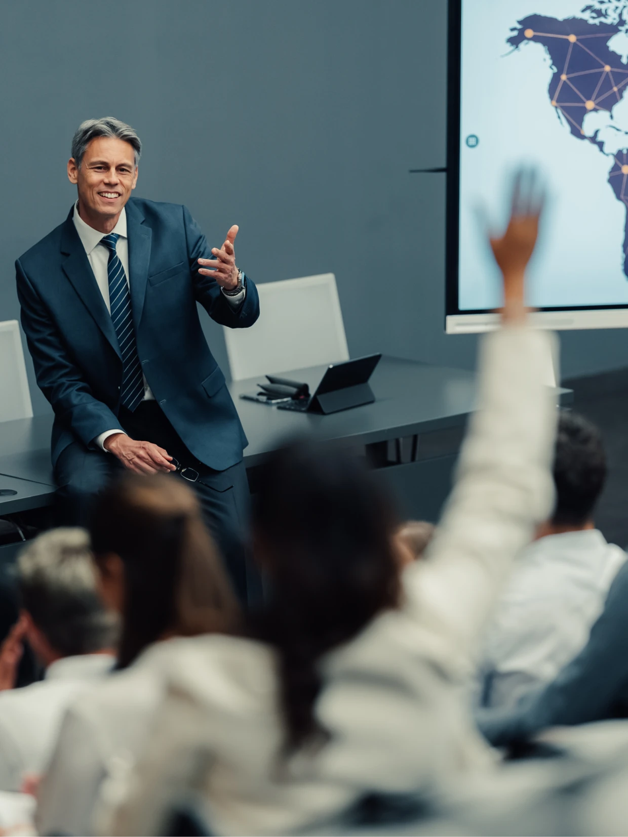 Man in a suit giving a presentation to a group of people sitting in chairs in front of a table